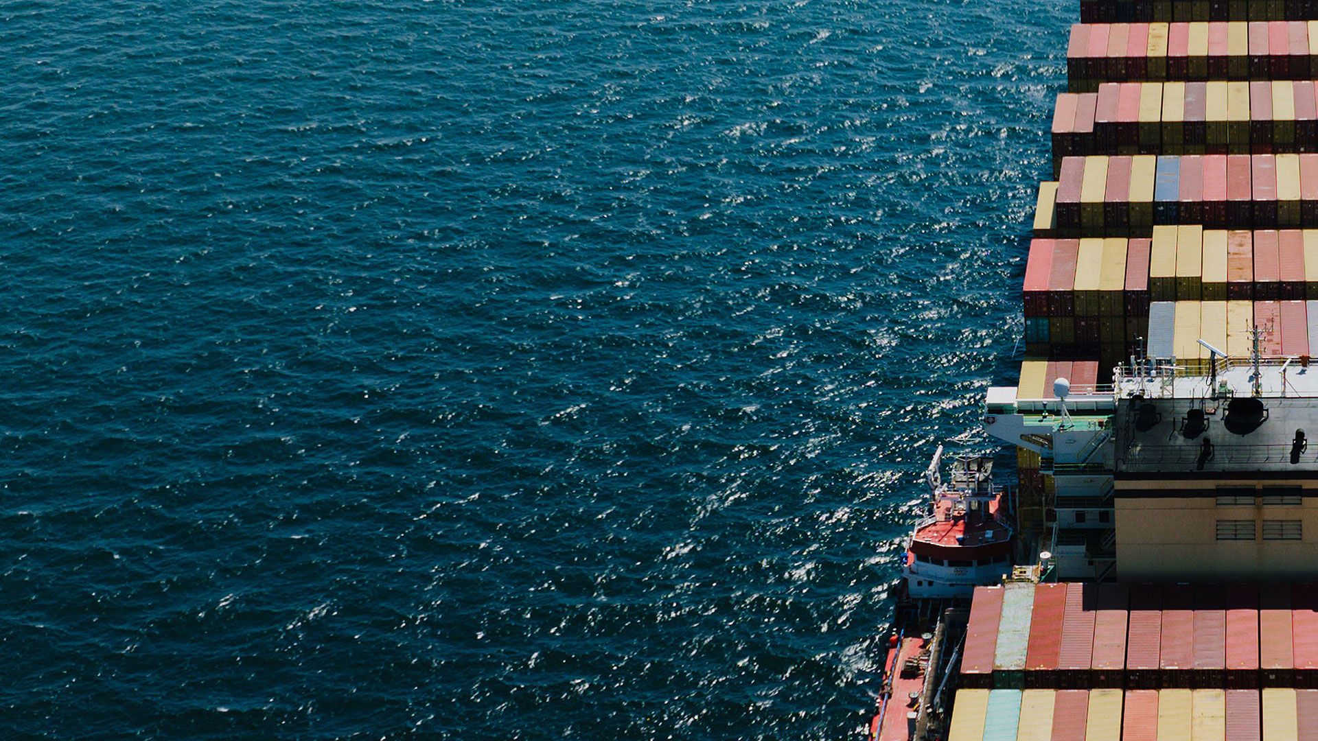 Container ship crossing azure waters. Aerial view: multicoloured containers stacked on deck.