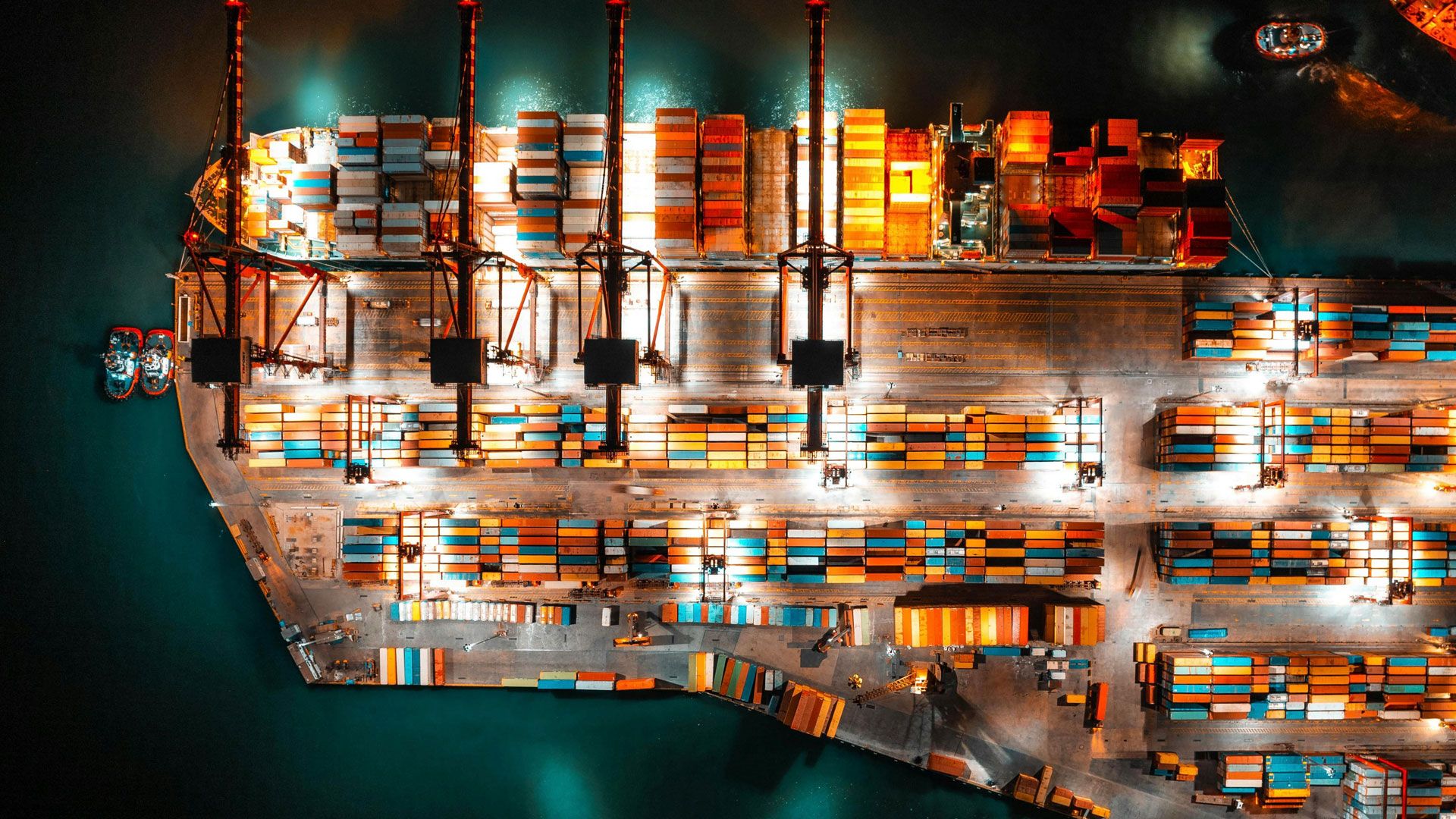 Farbige Container und ein Containerschiff an einem Terminal bei Nacht (verdeutlichen den globalen Handel, der auch bei Nacht weiterläuft)