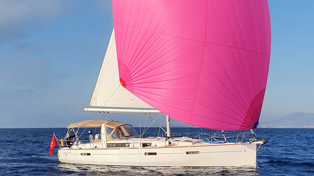 Un yacht battant pavillon suisse navigue avec une voile rose.