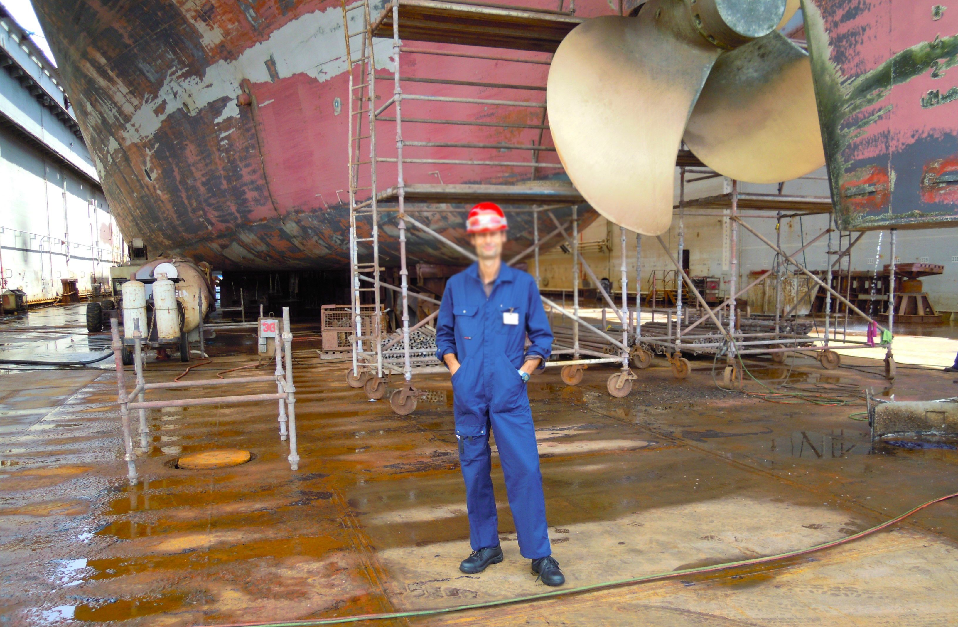 A worker in overalls stands in front of a commercial seagoing vessel, representing foreign seafarers.