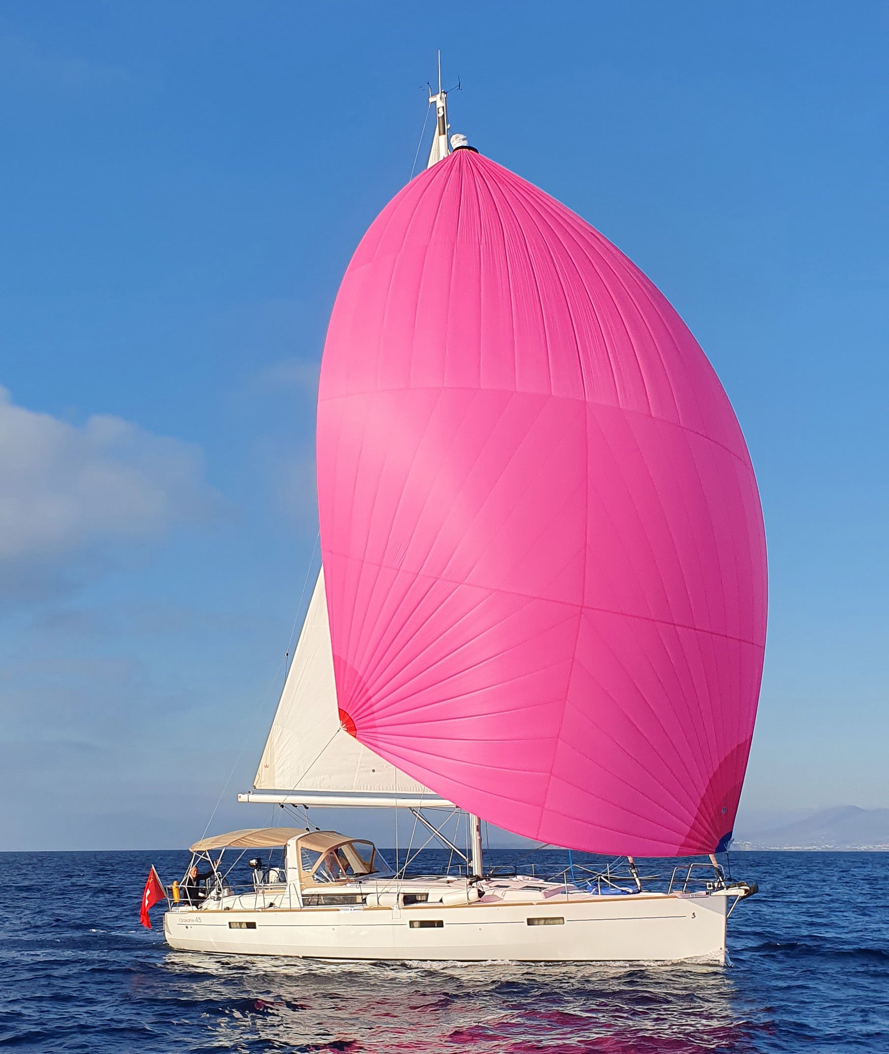 Un yacht battant pavillon suisse navigue avec une voile rose.